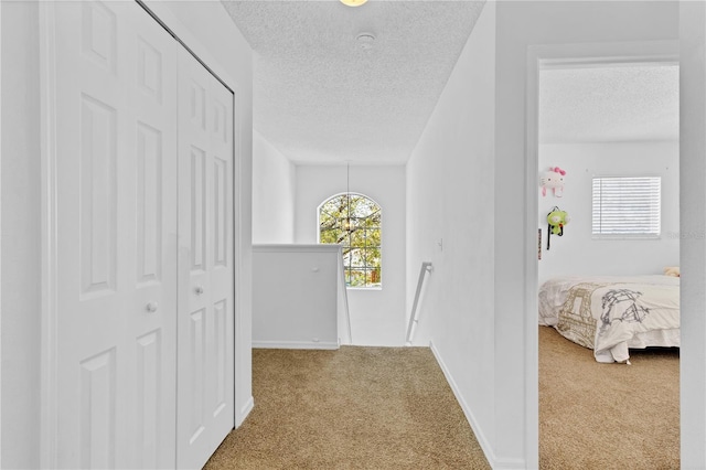 hallway with carpet, an upstairs landing, baseboards, and a textured ceiling