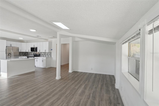 unfurnished living room featuring baseboards, dark wood finished floors, lofted ceiling, a sink, and a textured ceiling