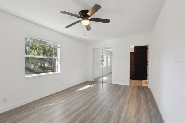 unfurnished bedroom featuring a textured ceiling, wood finished floors, a closet, baseboards, and ceiling fan