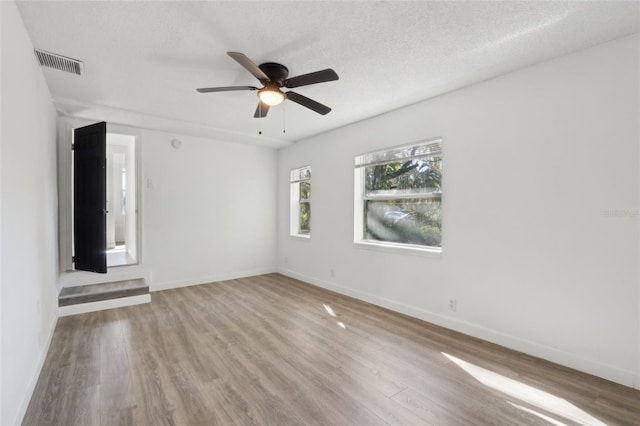 unfurnished room with visible vents, baseboards, wood finished floors, a textured ceiling, and a ceiling fan