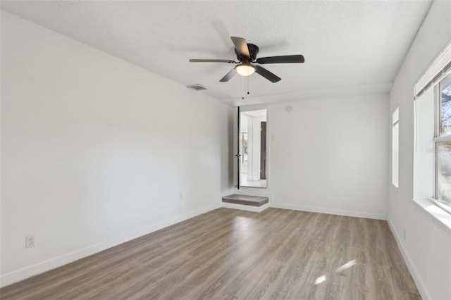 unfurnished room featuring visible vents, baseboards, wood finished floors, a textured ceiling, and a ceiling fan