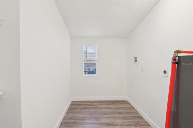 empty room featuring wood finished floors, baseboards, water heater, and a textured ceiling