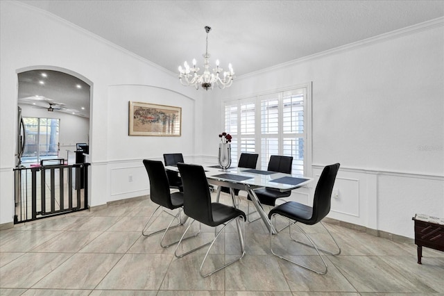 dining room featuring a wainscoted wall, light tile patterned flooring, arched walkways, ornamental molding, and ceiling fan with notable chandelier