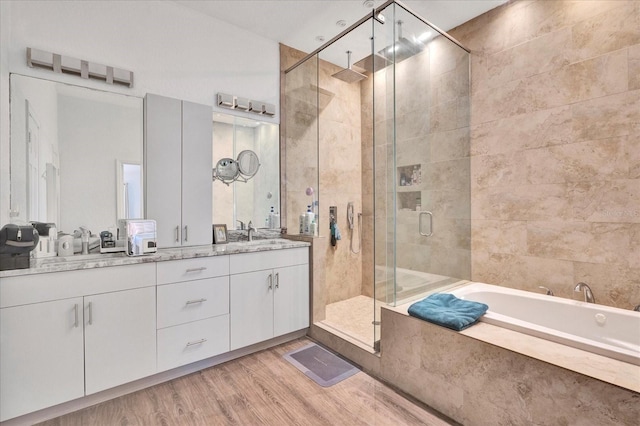 full bath featuring wood finished floors, double vanity, a sink, a shower stall, and a bath