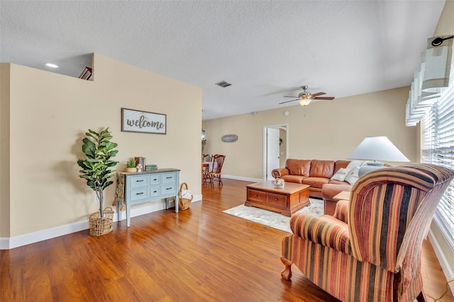 living area featuring visible vents, a textured ceiling, wood finished floors, and a ceiling fan
