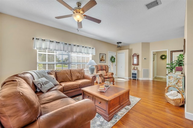 living area with a ceiling fan, visible vents, light wood finished floors, and a textured ceiling