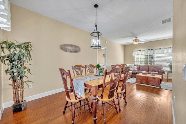 dining space with a ceiling fan, wood finished floors, visible vents, and baseboards