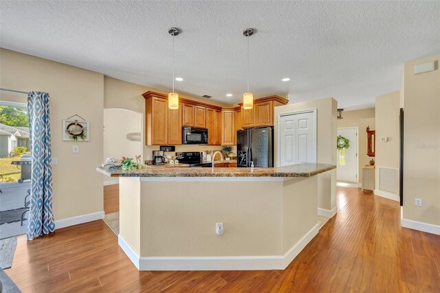 kitchen with light stone counters, visible vents, black appliances, and light wood-style floors