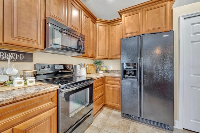 kitchen featuring light tile patterned floors, brown cabinets, black appliances, and light stone countertops