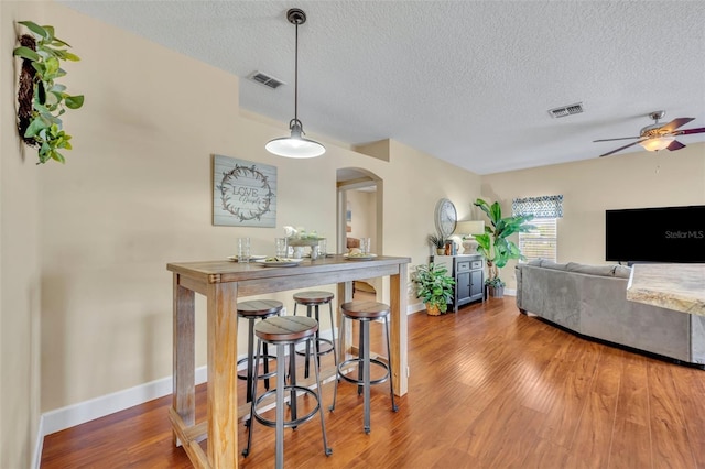 dining area with wood finished floors, arched walkways, visible vents, and ceiling fan
