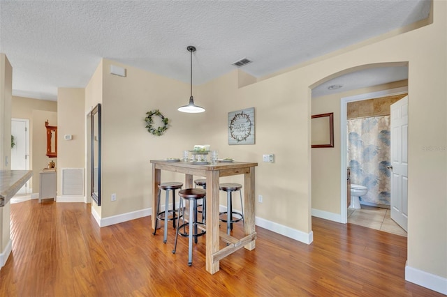 dining space featuring wood finished floors, visible vents, and arched walkways