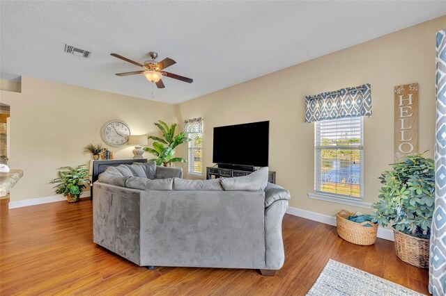 living area featuring plenty of natural light, a ceiling fan, visible vents, and light wood-type flooring