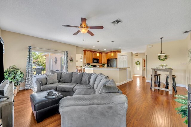 living room featuring visible vents, baseboards, light wood-type flooring, a textured ceiling, and a ceiling fan