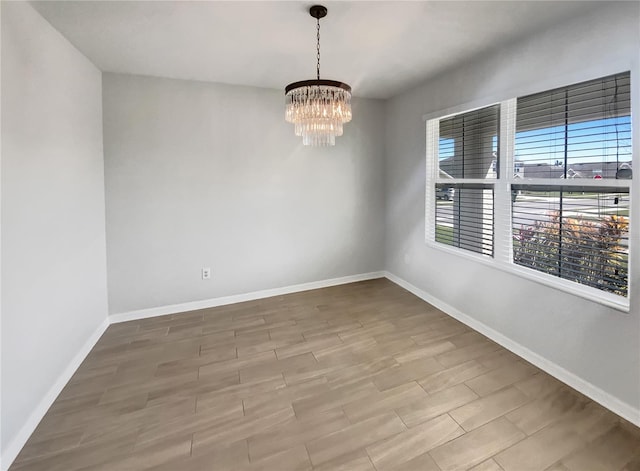 empty room featuring an inviting chandelier, baseboards, and wood tiled floor