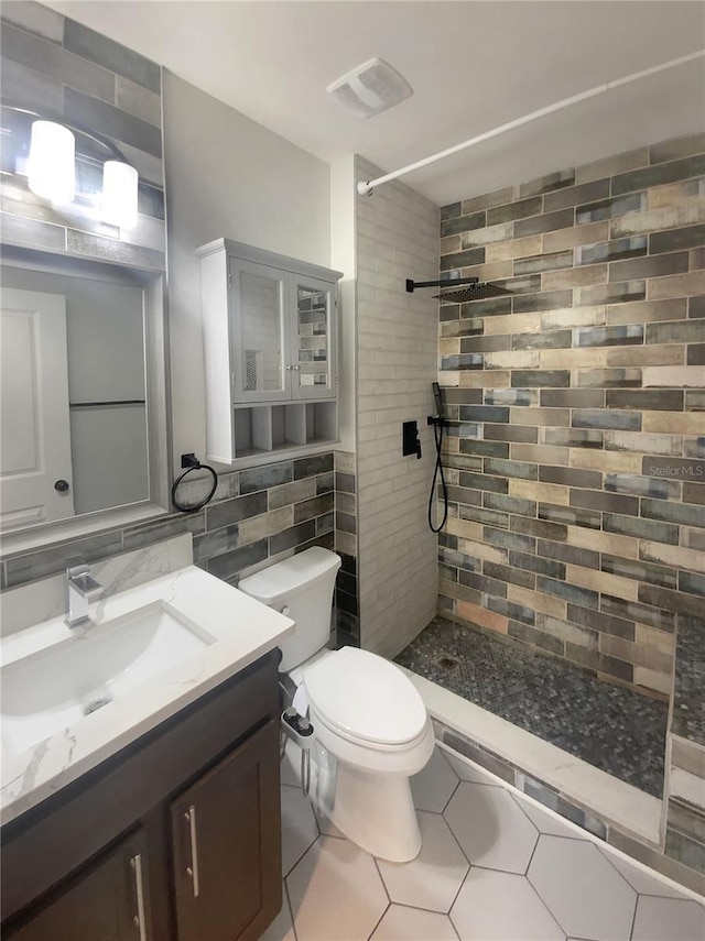 full bathroom with visible vents, tile walls, toilet, a tile shower, and vanity