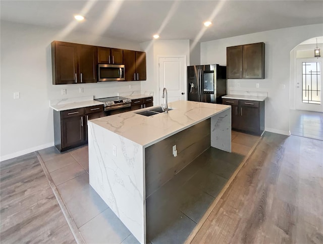 kitchen featuring dark brown cabinetry, recessed lighting, arched walkways, stainless steel appliances, and a sink