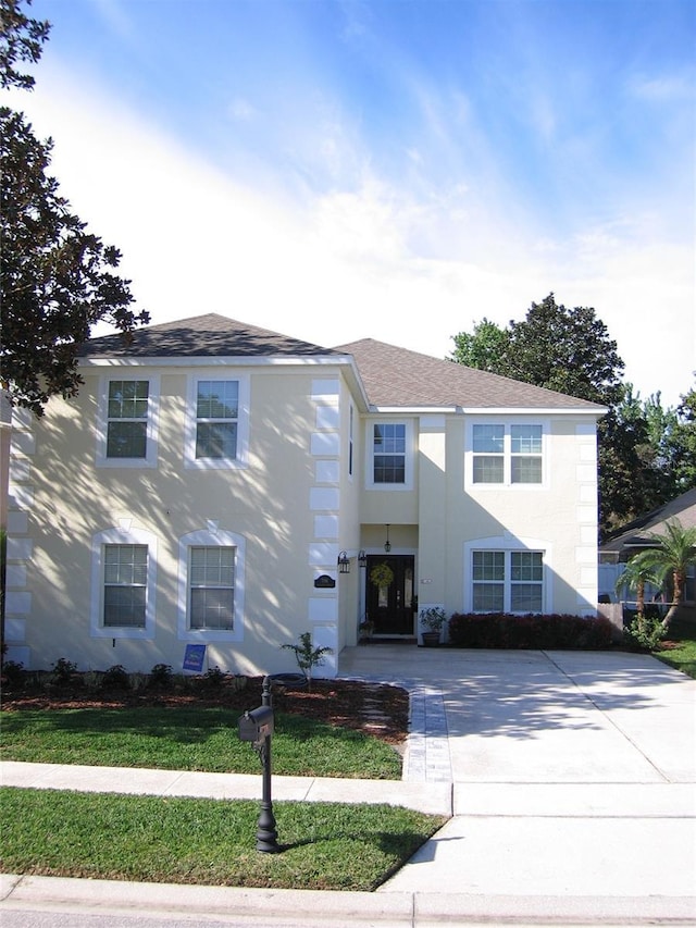 view of front of home featuring a shingled roof, a front lawn, driveway, and stucco siding