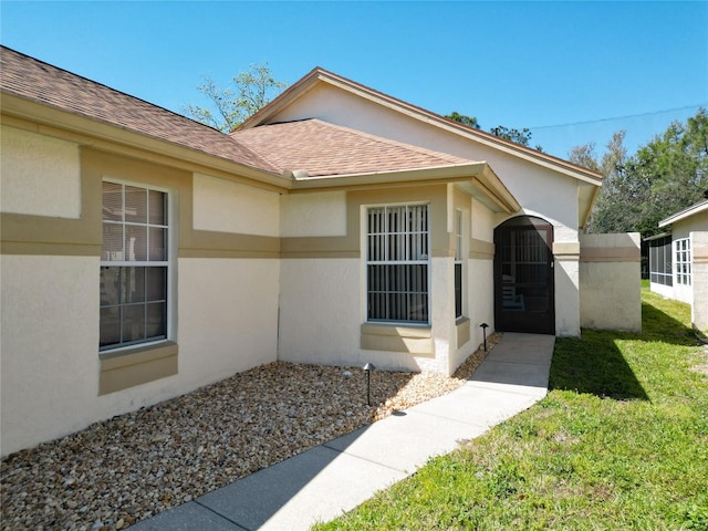 view of exterior entry with stucco siding, a shingled roof, and a yard