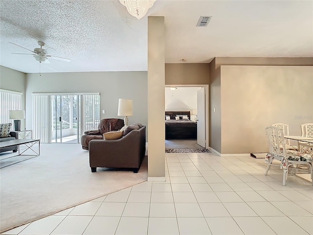 living room with light tile patterned floors, visible vents, ceiling fan, a textured ceiling, and light colored carpet