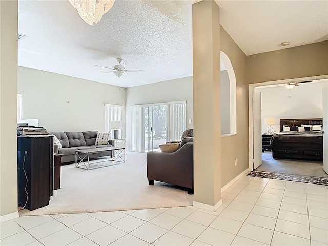 living area with light tile patterned floors, baseboards, arched walkways, ceiling fan, and a textured ceiling