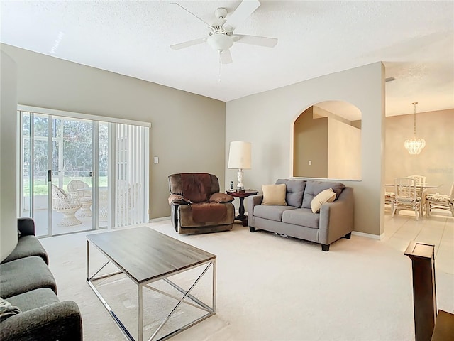 living room featuring carpet, baseboards, arched walkways, a textured ceiling, and ceiling fan with notable chandelier