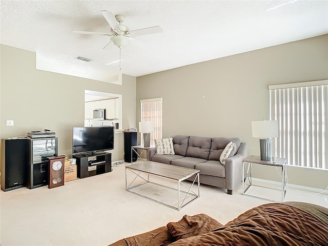 living area featuring a textured ceiling, light carpet, visible vents, and ceiling fan