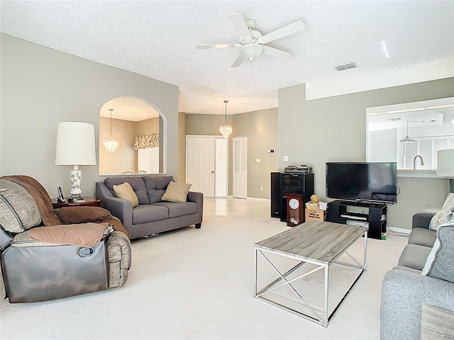 carpeted living room with a textured ceiling, arched walkways, visible vents, and ceiling fan