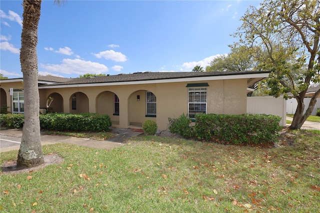 ranch-style home featuring stucco siding, a front lawn, and fence