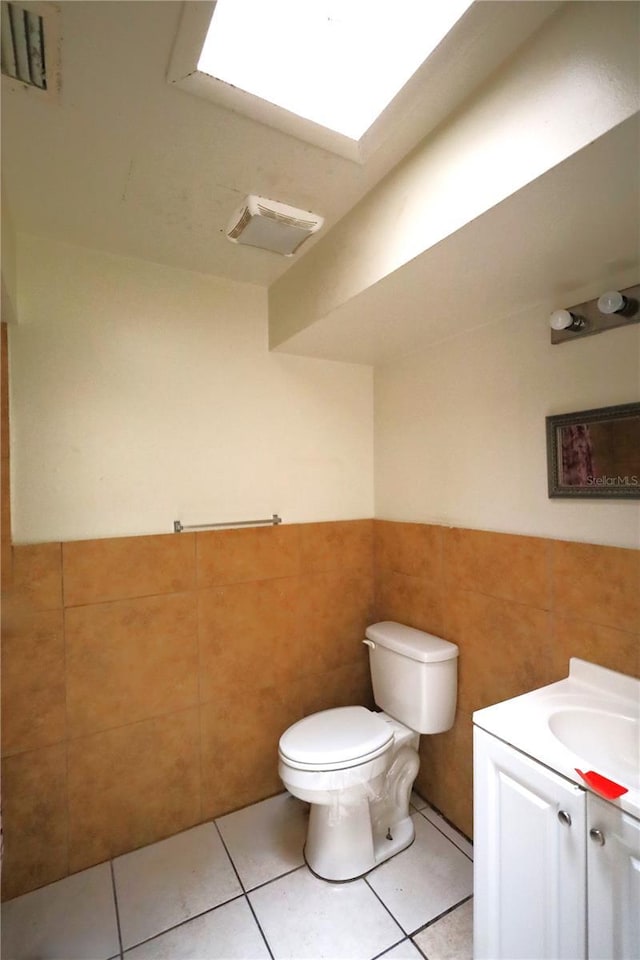 half bath with visible vents, toilet, tile walls, and wainscoting