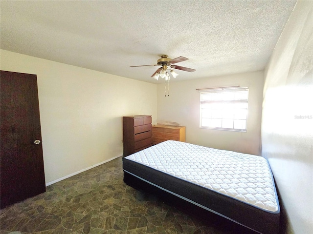 bedroom featuring a textured ceiling, stone finish flooring, baseboards, and a ceiling fan