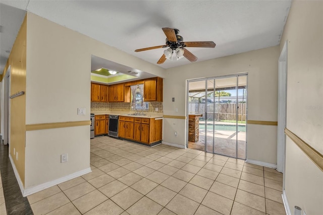 kitchen with brown cabinets, a tray ceiling, light countertops, dishwasher, and ceiling fan