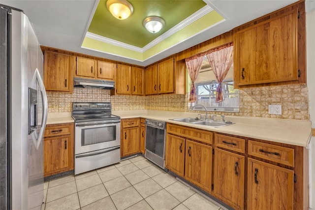 kitchen featuring under cabinet range hood, a tray ceiling, brown cabinets, stainless steel appliances, and a sink