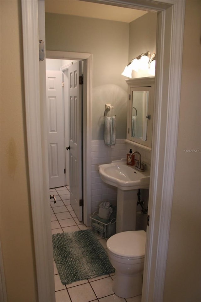 bathroom featuring tile patterned flooring, a wainscoted wall, toilet, tile walls, and a sink