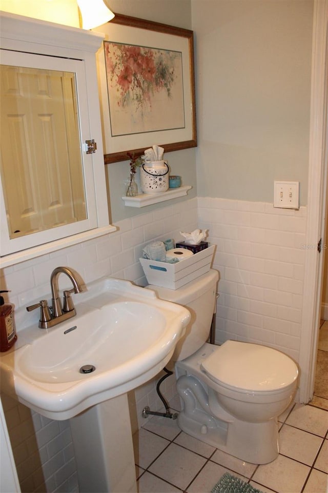 bathroom featuring tile patterned flooring, toilet, wainscoting, tile walls, and a sink