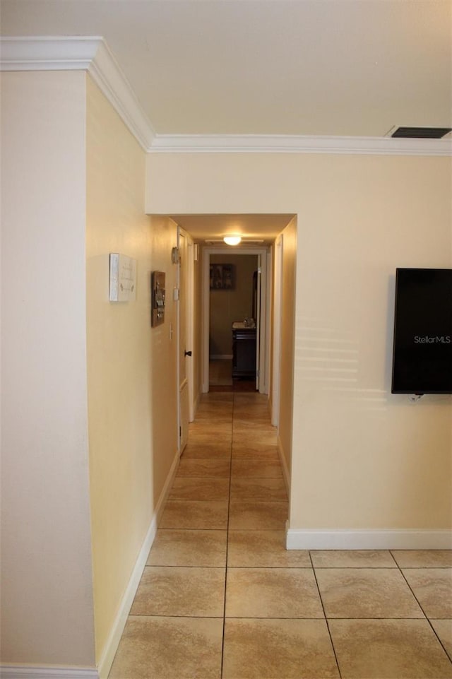 hallway featuring light tile patterned floors, visible vents, baseboards, and crown molding