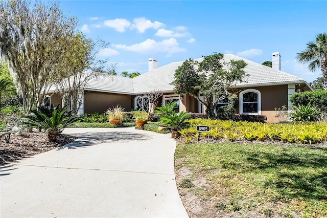 view of front of property featuring a tile roof, stucco siding, driveway, and a chimney