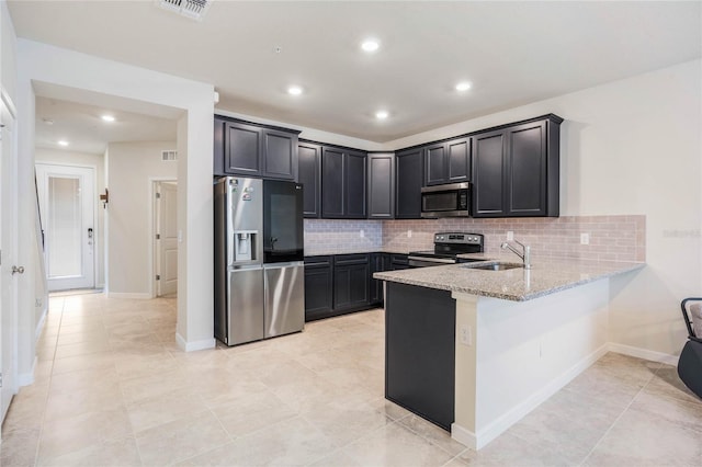 kitchen with a sink, backsplash, appliances with stainless steel finishes, a peninsula, and light stone countertops