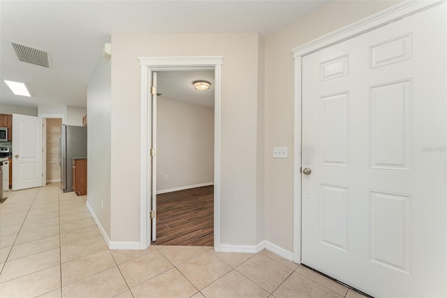 corridor with light tile patterned floors, visible vents, and baseboards