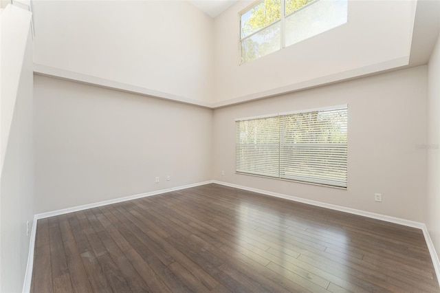 unfurnished room with baseboards, a high ceiling, and dark wood finished floors