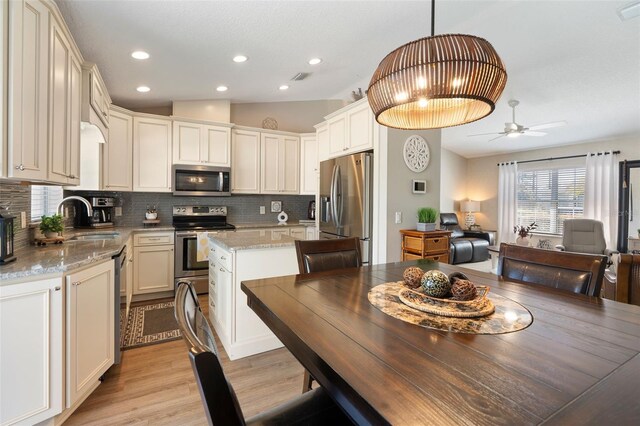 kitchen with backsplash, lofted ceiling, light stone counters, stainless steel appliances, and a sink