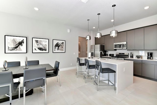 kitchen with decorative light fixtures, an island with sink, light countertops, a kitchen bar, and appliances with stainless steel finishes