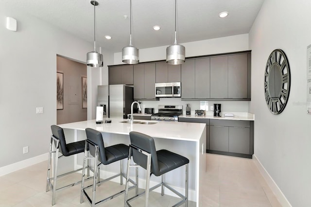 kitchen featuring gray cabinetry, stainless steel appliances, a kitchen breakfast bar, and a sink