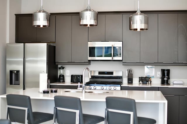 kitchen with a kitchen bar, gray cabinetry, decorative light fixtures, appliances with stainless steel finishes, and light countertops