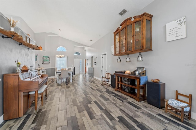 hall with visible vents, baseboards, wood finished floors, a notable chandelier, and high vaulted ceiling