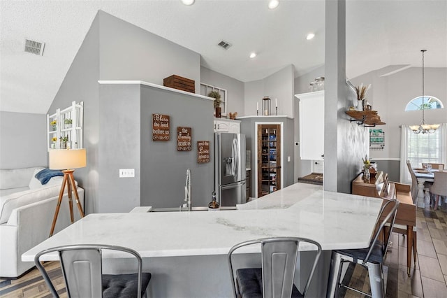 kitchen with visible vents, a breakfast bar, stainless steel fridge, an inviting chandelier, and vaulted ceiling