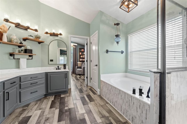 full bath featuring vanity, a garden tub, wood finished floors, and vaulted ceiling