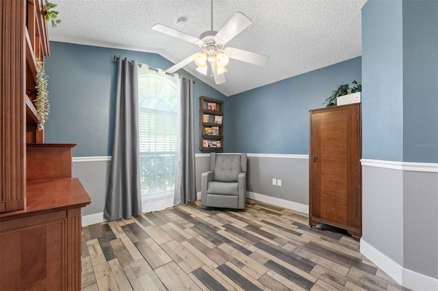 unfurnished room featuring lofted ceiling, a ceiling fan, a textured ceiling, wood finished floors, and baseboards