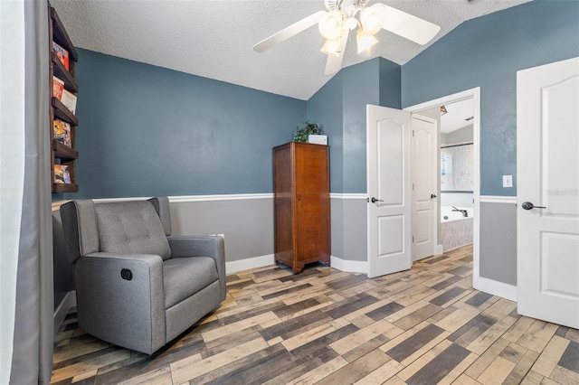 living area with a textured ceiling, wood finished floors, baseboards, ceiling fan, and vaulted ceiling