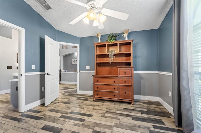 bedroom featuring wood finished floors, visible vents, baseboards, arched walkways, and a textured ceiling