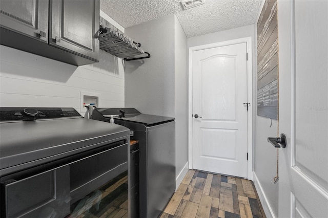 clothes washing area with wood finished floors, visible vents, washing machine and clothes dryer, cabinet space, and a textured ceiling